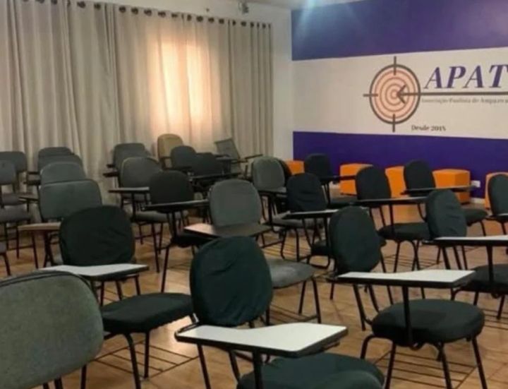 Vista do auditório da APAT com cadeiras com pranchetas e o painel da APAT.