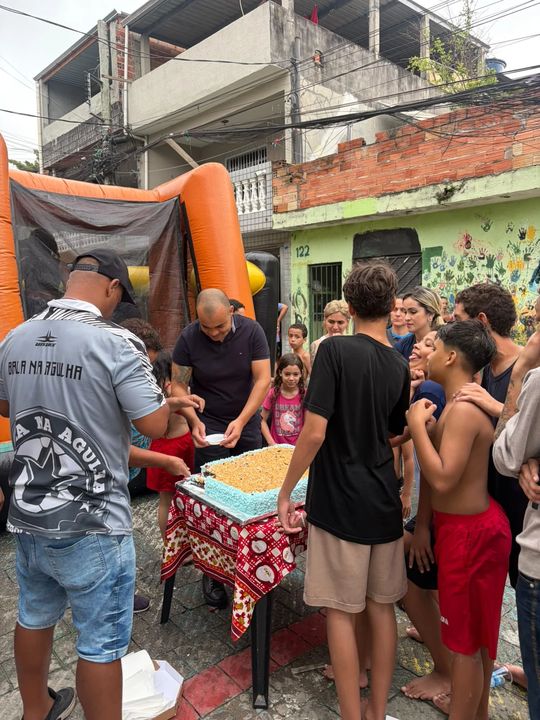 Bolo sendo cortado e servido às crianças na rua, ao lado do brinquedo inflável.