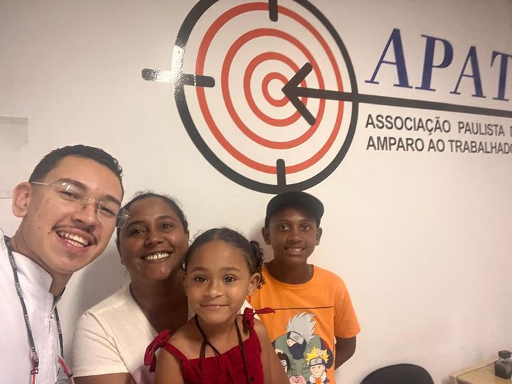 Família atendida pelo projeto Salvando Sorrisos, em frente ao logotipo da APAT.