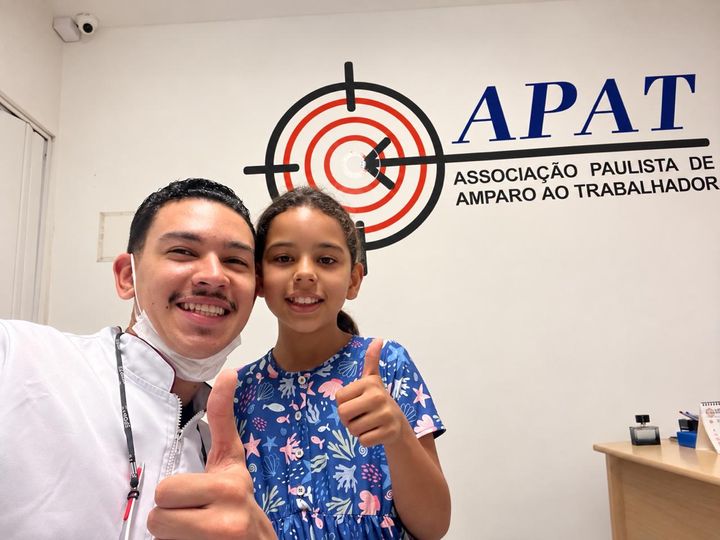Dentista do projeto com uma criança atendida, fazendo sinal de positivo.